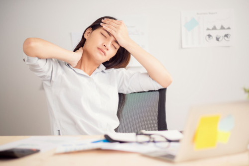 Young woman at laptop with headache, holding her neck and head